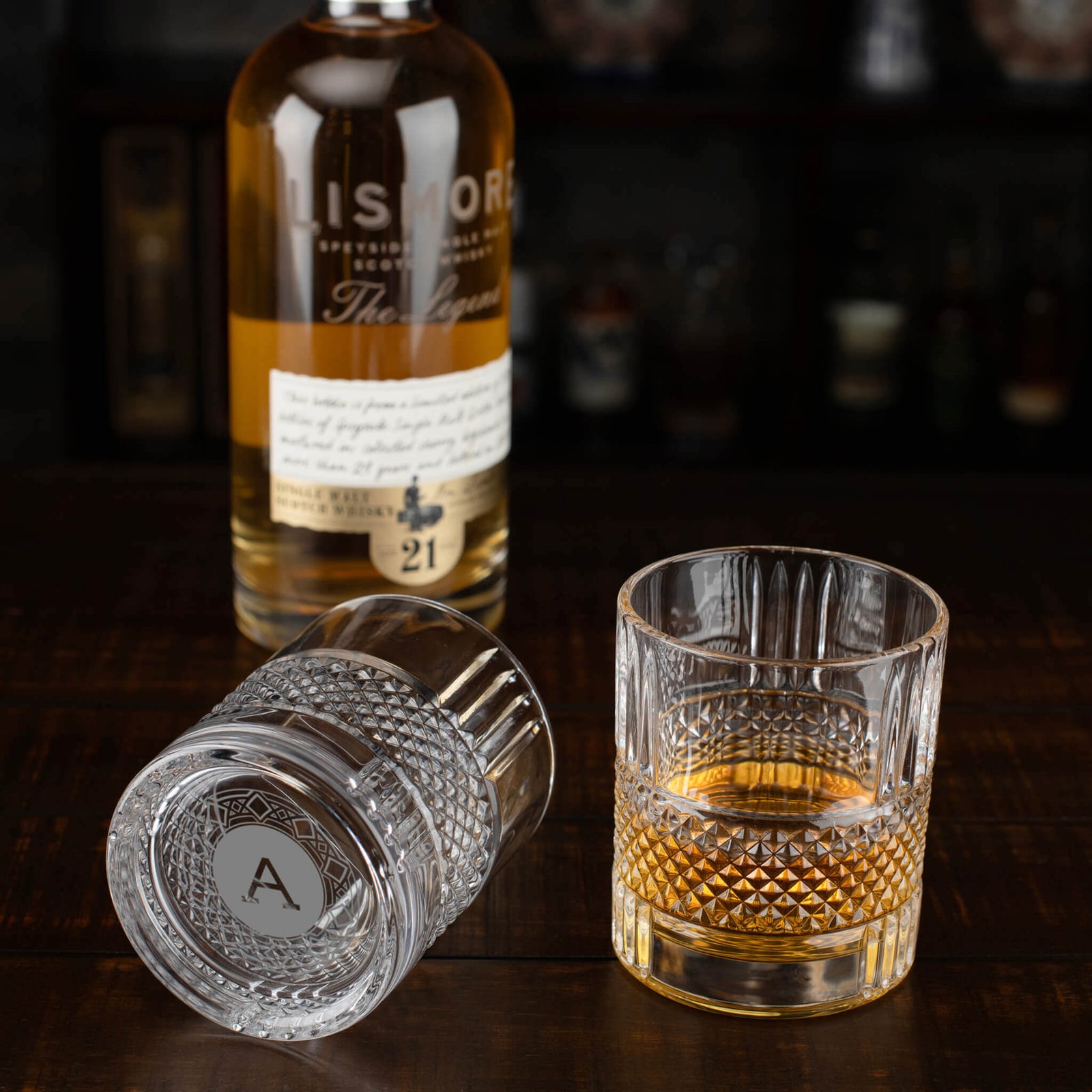 Personalized whiskey glasses with engraved initials beside a bottle of scotch—stylish and functional wedding favors.