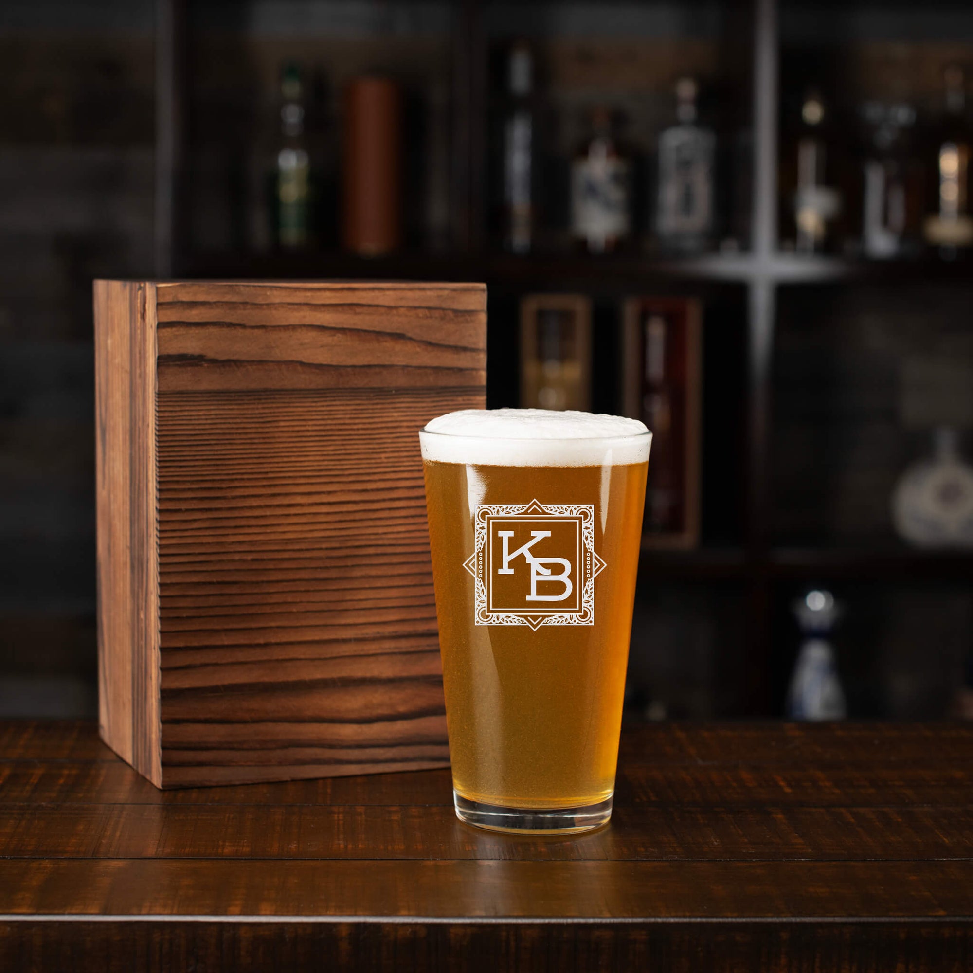 Personalized pint glass with blueprint-inspired monogram beside a sleek wooden box – a stylish gift for architects who love design and craft beer.