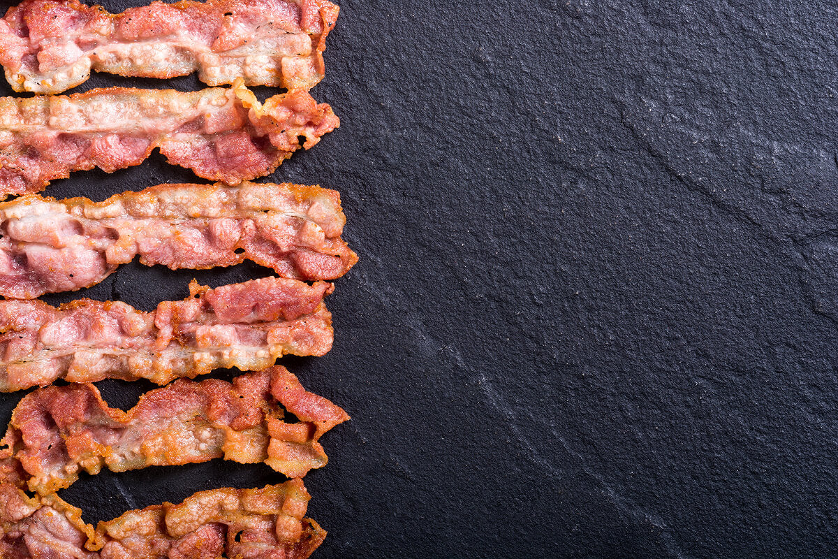 Crispy bacon strips arranged on a dark slate background — bold butcher gift inspiration.