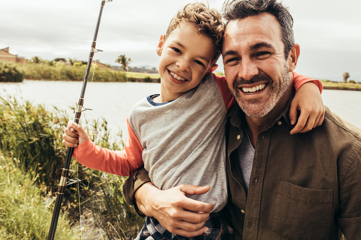 A fisherman and his young helper, smiling big by the water’s edge — where the only thing better than the catch is the snack they’ll share after.