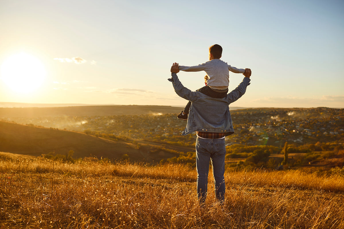 Dad celebrating at sunset with child on shoulders—perfect visual for a bold birthday card like The Meat Card™ that delivers more than just words.