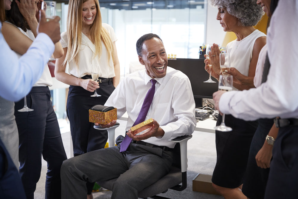 Office man surrounded by coworkers celebrating his birthday and opening a gift box