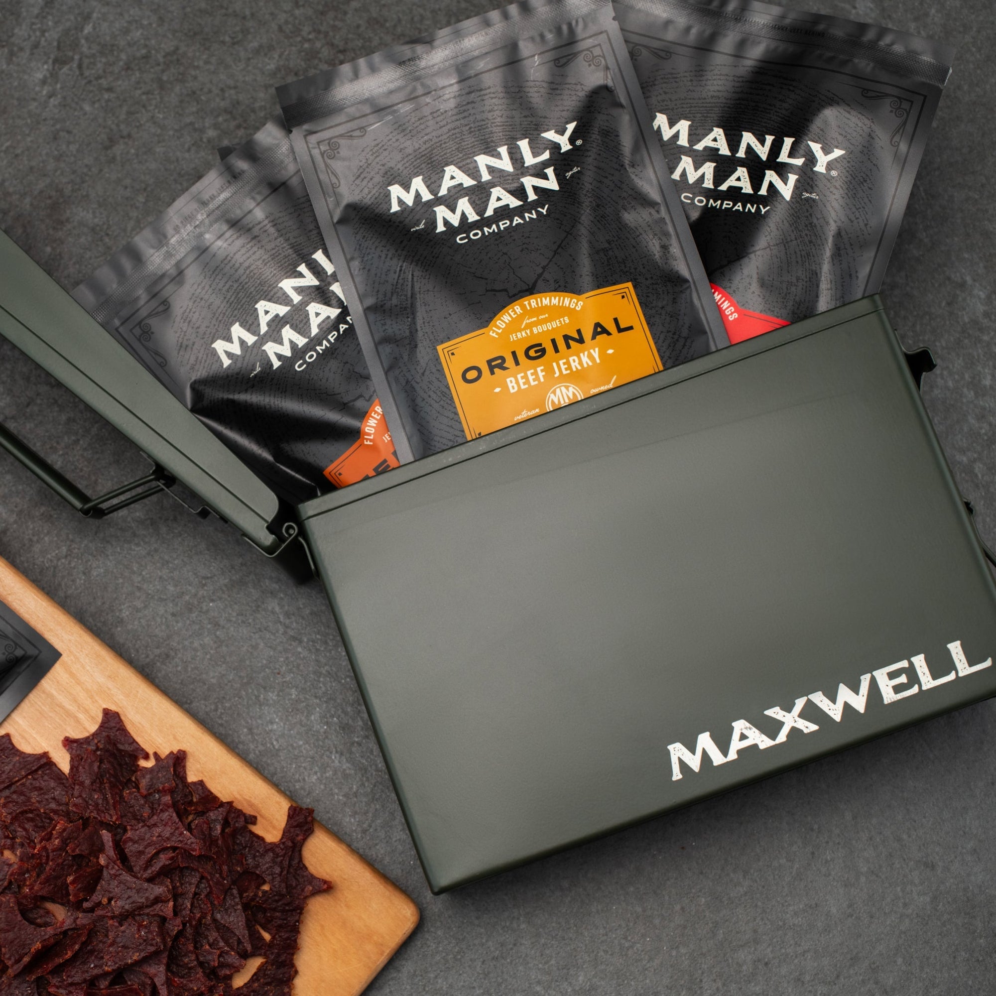 A rugged and personalized gift featuring a green ammo can filled with assorted beef jerky packs from the Manly Man Company. Perfectly paired with jerky pieces on a wooden board, it’s a bold and unique gift idea.