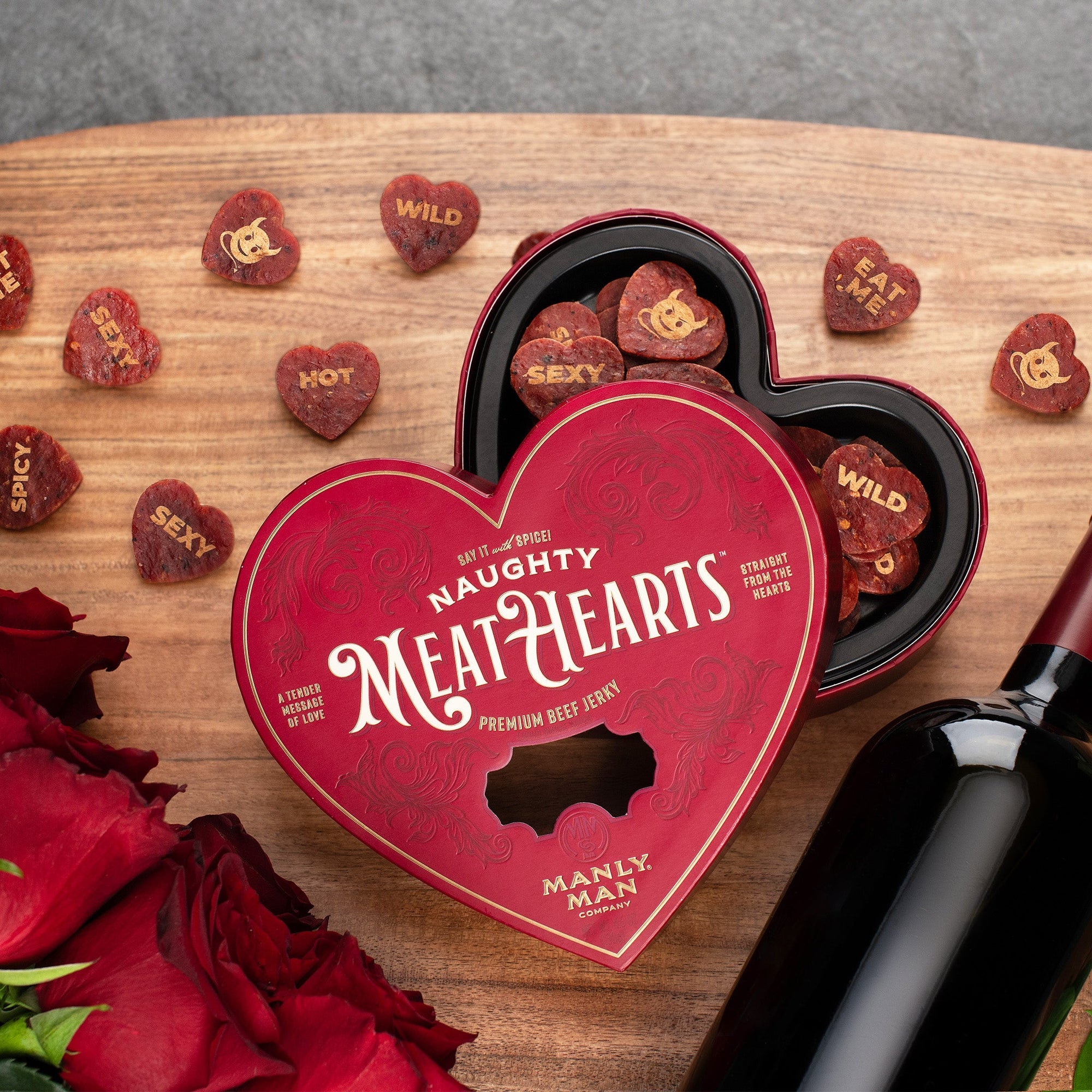 A heart-shaped red box labeled 'Naughty MeatHearts' featuring premium beef jerky, surrounded by heart-shaped jerky pieces with playful messages like 'Hot,' 'Sexy,' 'Eat Me,' 'Spicy,' and 'Wild,' displayed on a rustic wooden surface