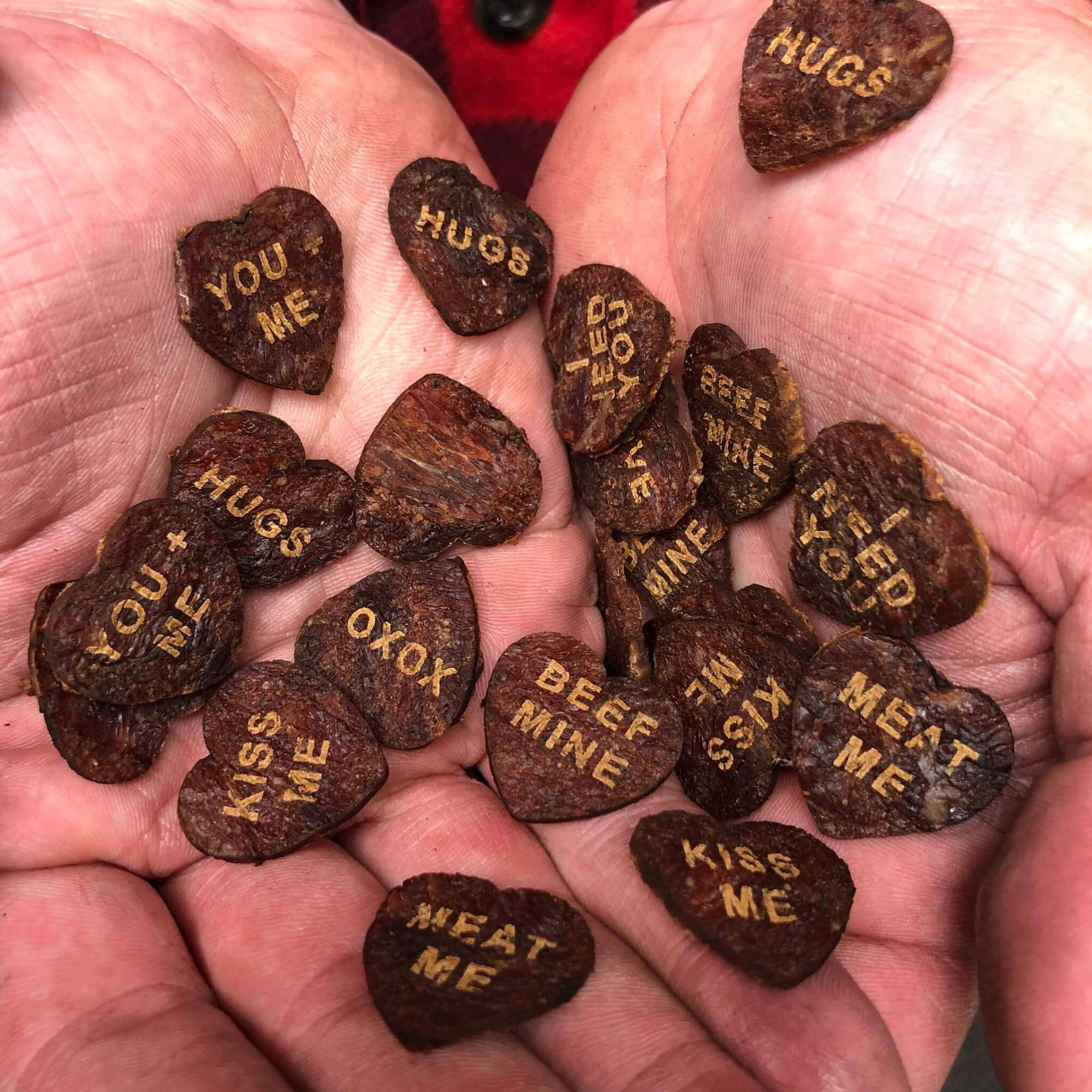 Over one dozen mini beef jerky hearts being held in the palms of two hands