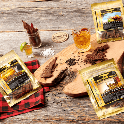 Three individual bags of jerk next to piece of beef jerky, sitting on wood campground table