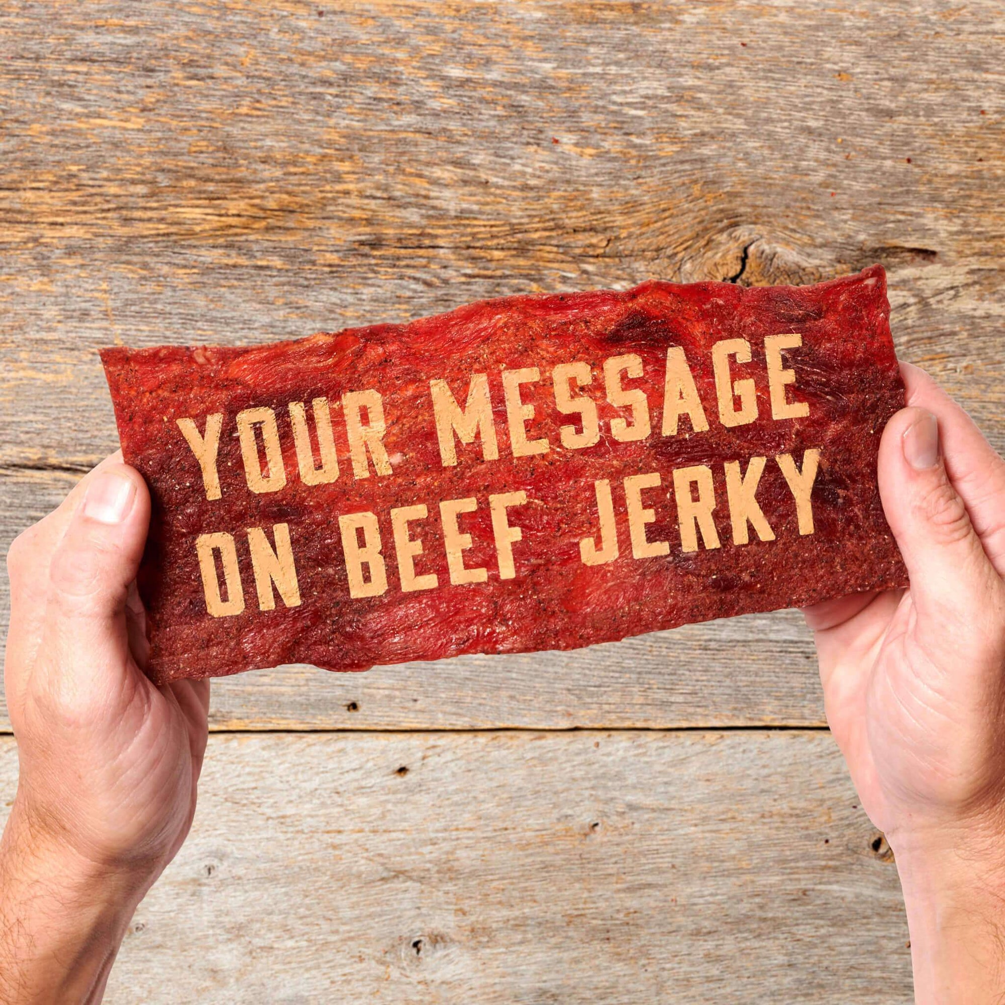 Custom edible meat greeting card that says "your message on beef jerky" and held by two hands, in front of wood panel background
