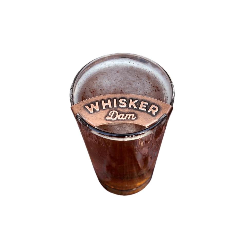 Copper whisker dam affixed atop pint glass filled with beer on white background
